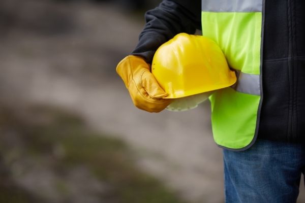 closeup of a man wearing a construction vest and holding a hardhat