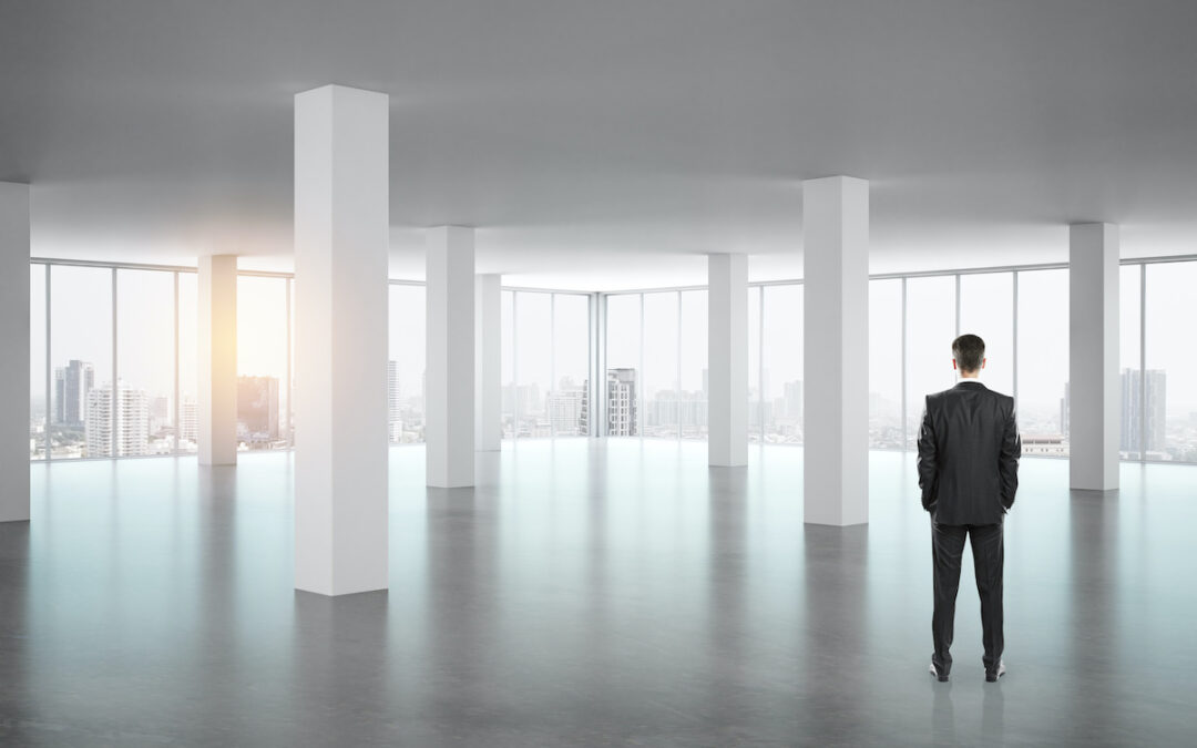 Businessman standing in empty office interior with panoramic window, new york city view and daylight
